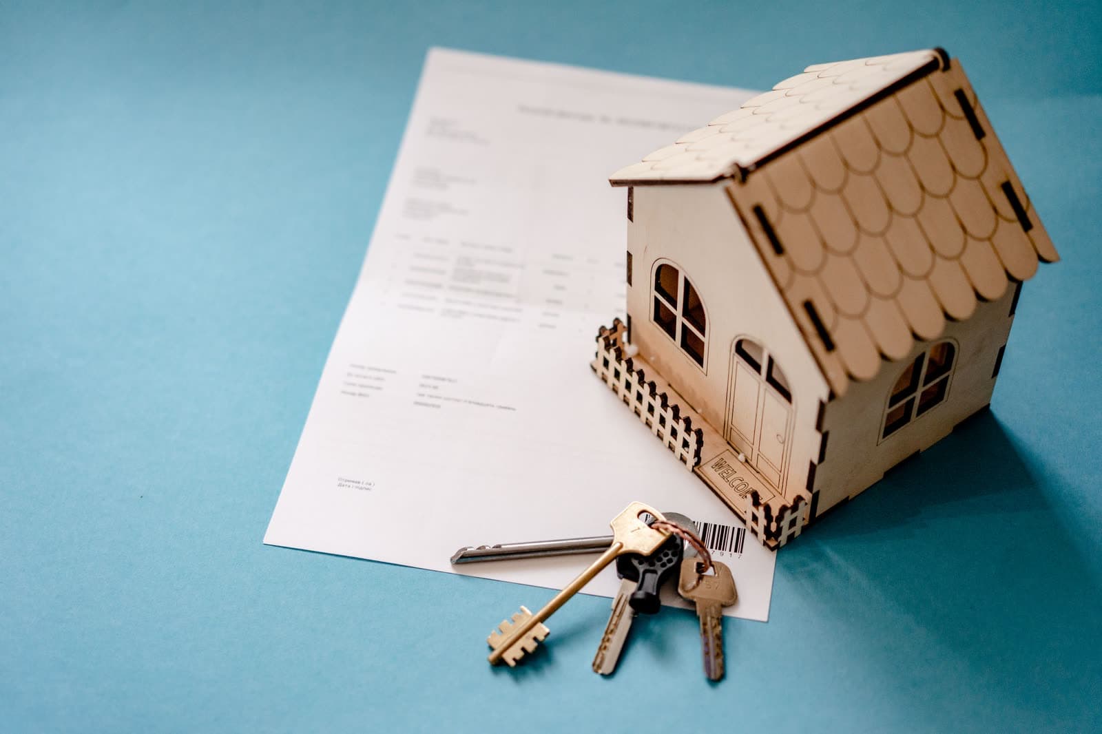 A small wooden house model and a set of keys resting on a printed contract